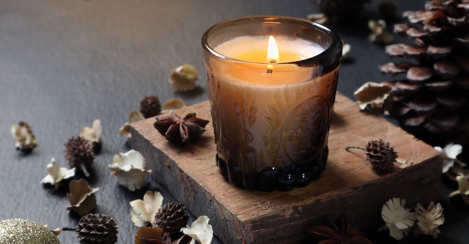 nice aromatic scented candle glass is lighting on the wooden holder on black wooden table with dried flowers , herbs and spices pinecone in the living room during Christmas new year party happy family