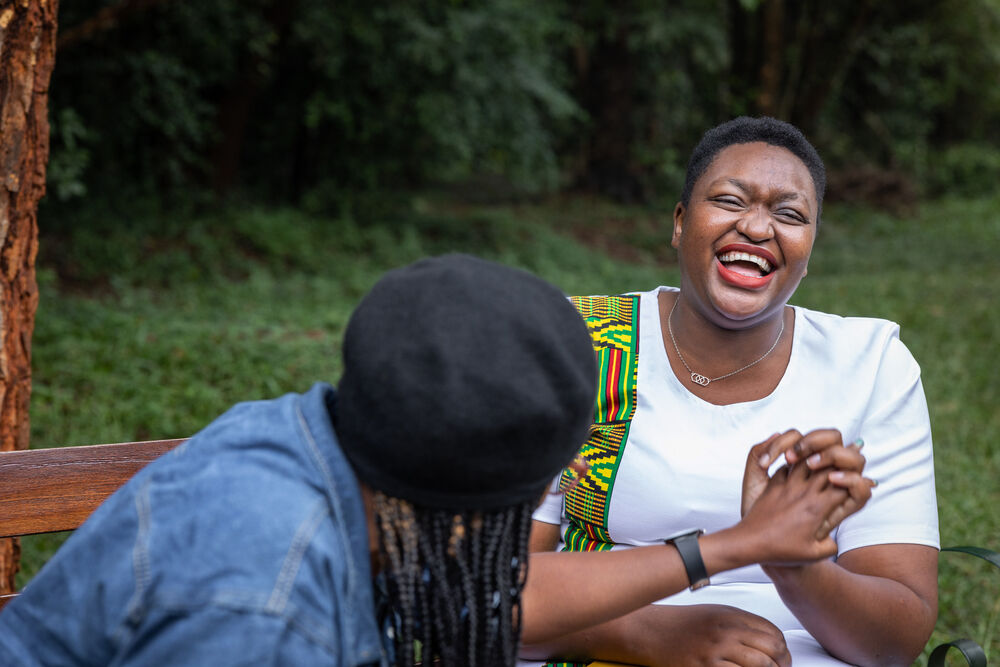 Two friends enjoying a laughing while having a conversation on a park bench in Nairobi, Kenya, the woman on the right is living with HIV
