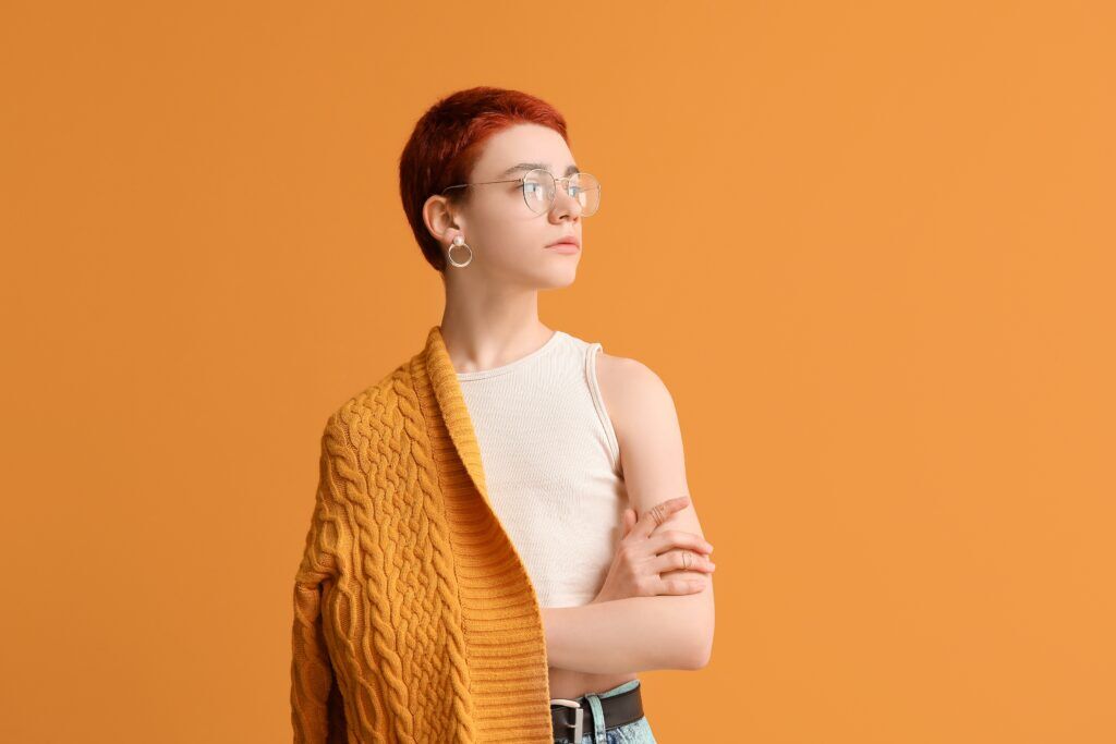 a nonbinary (FLINTA) person wearing an orange sweater and white crop top in front of an orange wall